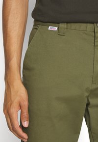 Pantaloni verde oliva con una texture liscia, dotati di un'etichetta Tommy Jeans in vita e un design semplice e su misura.