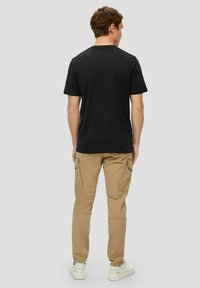 Black cotton T-shirt with a round neckline, paired with khaki cargo pants featuring side pockets, and white sneakers on a grey background.