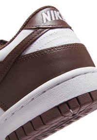 Smeđi kožni tenisice s bijelim akcentima i teksturiranim površinama, s istaknutim Nike logom i gumenim potplatima za dobar grip.