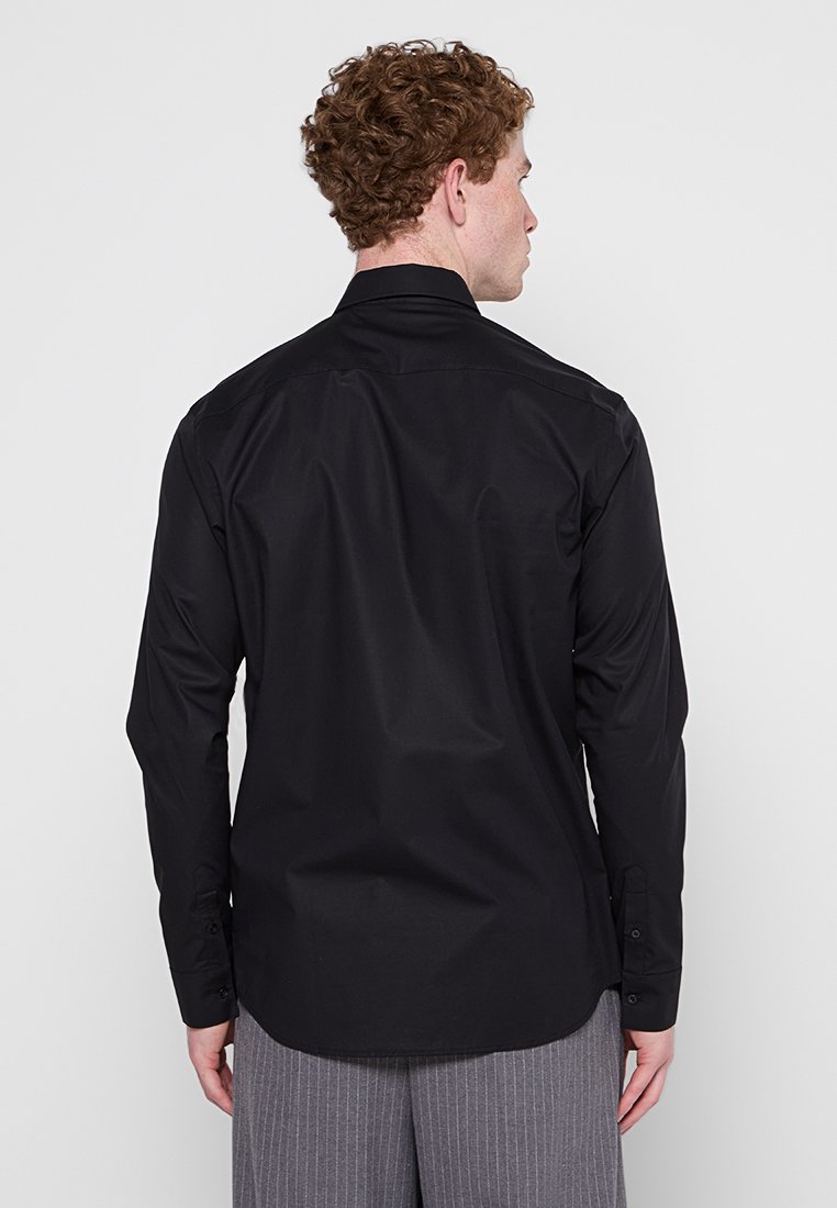 Chemise noire à manches longues en tissu lisse, avec un col standard et des poignets boutonnés, un ourlet arrondi et un design minimaliste.
