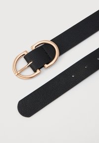 Sort tekstureret læderbælte med en rund guld dobbelt-ring spænde og fem justeringshuller på en hvid baggrund.