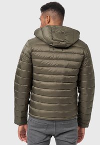 Chaqueta acolchada verde oliva con capucha, que presenta secciones acolchadas horizontales y un logo en el brazo izquierdo. Tejido suave y resistente al agua.