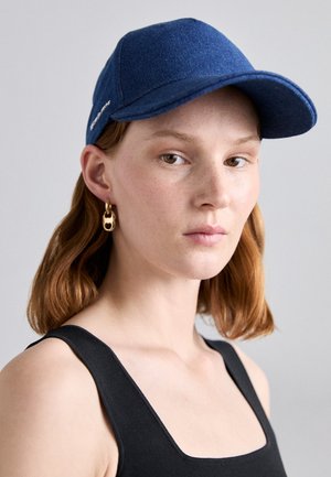 Casquette bleue au design structuré, fabriquée en tissu avec une texture lisse. Elle présente une visière courbée et des accents de couture, accompagnée de boucles dorées.