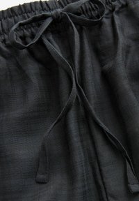 Pantalons en lin noir avec une taille élastique et un cordon de serrage noué. Le tissu a une texture et une apparence légèrement froissée.