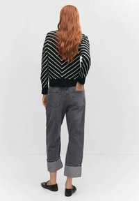 Un pull en tricot à motifs en chevrons noir et blanc, associé à un jean en denim gris, avec des poignets roulés et une coupe décontractée. Des ballerines noires complètent le look.