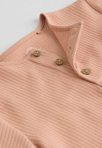 Soft pink ribbed fabric with three wooden buttons fastened along a folded edge, showing stitching and texture detail.