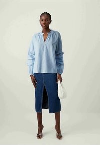 Gaiši zila svītraina blūze ar V-veida izgriezumu un savilktu kakla daļu, saskaņota ar džinsu svārkiem ar priekšējo šķēlumu un baltu somu.