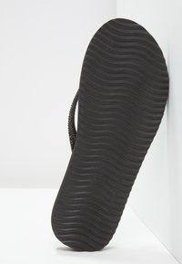 Black flip-flop sole with a textured, wavy pattern; made of rubber, featuring a minimalist design and a curved shape.