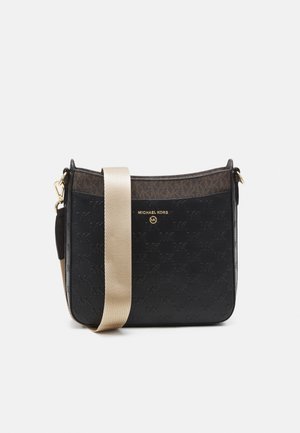 Czarna torebka typu crossbody Michael Kors z wytłaczanym wzorem logo, złotymi literami i szerokim beżowym regulowanym paskiem na jednolitym tle.