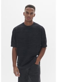 Tricou negru texturat cu mâneci scurte, guler rotund și un model discret de dungi orizontale, asortat cu blugi închiși la culoare.