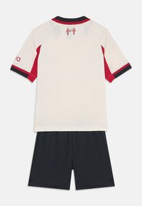 Set dresov in šortih. Kremasta majica z rdečimi detajli in mornarsko modrim obrobjem; črne šortke. Vsebuje vezenine logotipa na hrbtu.