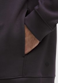 Mørkegrå sweatshirt med blød tekstur, med en sidelomme og ærmeafslutninger. Indeholder en lille logodetalje ved kanten.