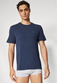 T-shirt azul marinho de manga curta, feito de um tecido texturizado, com um decote redondo e um discreto detalhe de logotipo no peito, combinado com calções cinzentos.