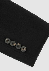 Mustast villast kangas pehme tekstuuriga, millel on mansetinupu serval neli tumedat nuppu. On ka õmbluseid detailidena nähtavad.