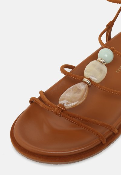Sandale marron à lanières avec semelle en cuir lisse et perles décoratives vert clair et beige sur les lanières supérieures.