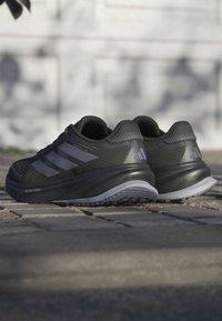 Zwarte sportieve schoenen met een textuur bovenkant, drie reflecterende strepen, een gevoerde tussenzool en een rubberen buitenzool, met een gestroomlijnd ontwerp.