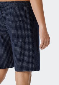 Calzoncillos de color azul marino con un patrón de puntos, cinturilla elástica y bolsillo lateral, que presentan una textura suave y un ajuste relajado.