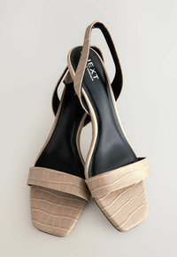Escarpins ouverts beiges avec un motif crocodile, une large courroie sur le devant et une semelle intérieure noire. Design de talon carré et style slingback.