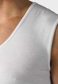 Biała bezrękawnik z głębokim dekoltem w kształcie litery V. Wykonany z gładkiego, lekkiego materiału, z czystym wykończeniem brzegów.