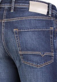 Dark blue denim jeans featuring a back pocket with double-stitch detailing and a light gray leather patch above the waistband.