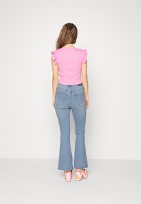 Vaaleanpunainen istuva paita, jossa on rypytyslehdet, yhdistettynä vaaleansinisiin leveälahkeisiin farkkuihin ja kukkakuosisilla koroketossuilla. Yksinkertainen tausta.