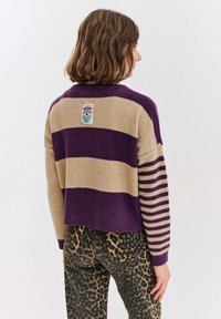 Pletený svetr s přerušovanými fialovými a béžovými pruhy, krátký střih a visačkou vzadu. Kombinován s kalhotami s leopardím vzorem.