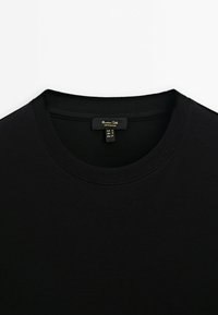 Schwarzes Baumwoll-T-Shirt mit rundem Ausschnitt und kurzen Ärmeln. Enthält ein Etikett mit der Größe (S) und Pflegeanweisungen. Weiche Textur.