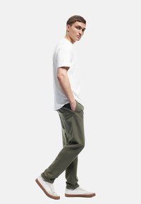 Hvid kortærmet t-shirt kombineret med olivengrønne sweatpants i en afslappet pasform. Brune og hvide sneakers fuldender outfittet.
