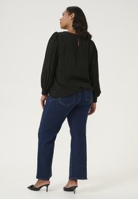 Blouse noire plissée avec des manches bouffantes et un détail en trou de serrure au dos, assortie à un jean droit bleu marine et des mules à talons noires.