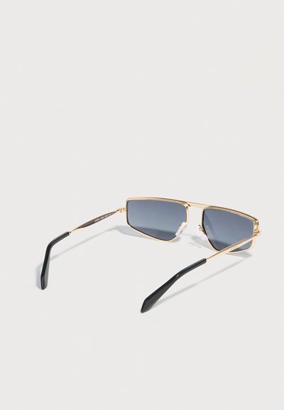 Χρυσά ορθογώνια γυαλιά ηλίου με σκούρα φακούς και μαύρες άκρες στα πλαϊνά, τοποθετημένα σε απλό ανοιχτό φόντο.