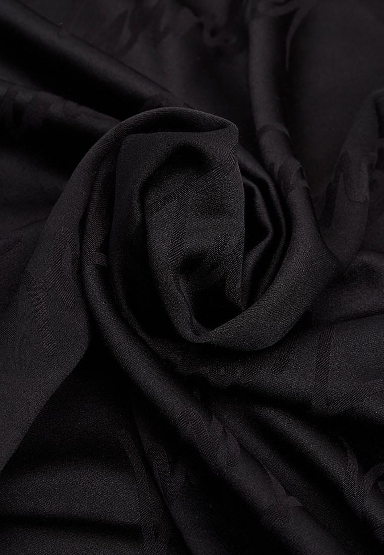 Czarna tkanina o miękkiej, gładkiej teksturze z subtelnym wzorem. Materiał jest luźno zawieszony i skręcony, ukazując głębię i wymiar.