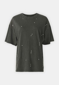 Camiseta de algodón negra de corte holgado, con mangas cortas y tachuelas metálicas esparcidas por la tela. Diseño de cuello redondo.