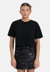 Zwarte cropped t-shirt met korte mouwen, ronde hals, gemaakt van zachte stof. Gecombineerd met een glanzende zwarte minirok met krokodillenstructuur.
