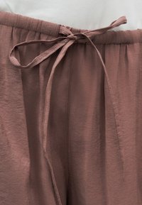 Κοντινό πλάνο σε παντελόνι από ύφασμα μαβί με ελαστική μέση και κορδόνι δεμένο σε φιόγκο στο κέντρο μπροστά.