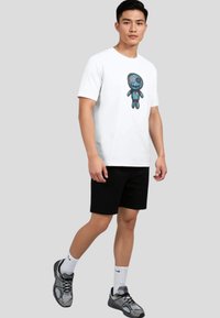 Camiseta blanca con un estampado de personaje de dibujos animados colorido, combinada con pantalones cortos negros y zapatillas grises. Diseño simple y casual.