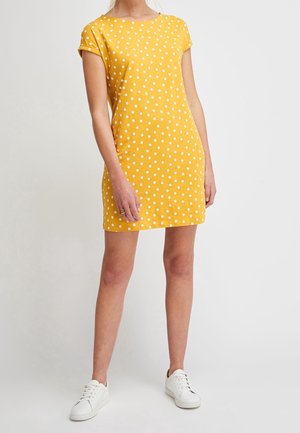 Żółta sukienka z krótkim rękawem w białe kropki. Wykonana z lekkiego materiału, z okrągłym dekoltem i luźnym fasonem. Noszona z białymi trampkami.