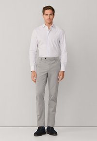 Pantaloni grigi chiari abbinati a una camicia bianca con bottoni caratterizzata da sottili righe, indossati con scarpe scamosciate blu scuro.