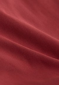 Rode stof met een gladde textuur en een fijne, gelijkmatige weving. Een lichte glans en valt zachtjes met zichtbare lichtreflecties.