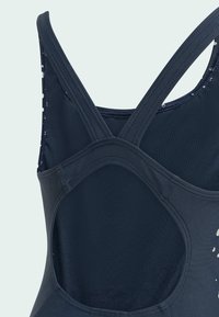 Maillot de bain bleu marine avec des bretelles croisées, un dos en découpe arrondie et une finition texturée ; présente des motifs abstraits légers dans des couleurs contrastées.