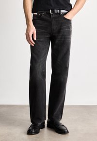 Jeanși din denim negru cu croială dreaptă, detalii ușor decolorate și design cu cinci buzunare, asortați cu pantofi din piele negri și o curea.