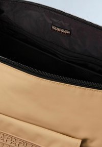 Borsa sintetica beige con superficie texturizzata, dotata di zip nera e interno nero. Etichetta del logo visibile all'interno, insieme a una tasca in rete.