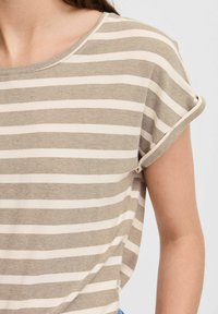 T-shirt rayé en beige clair et blanc, fabriqué en matériau doux, avec des manches courtes roulées et un col rond.