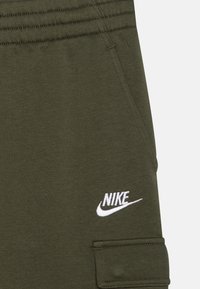 Olivgröna Nike sweatpants med elastiskt midjeband, sidoficka, fack med lock på cargofickan och vit broderad Nike-logga.
