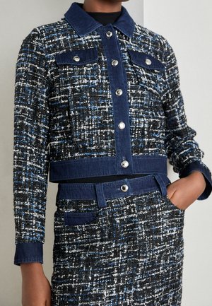 Veste en tweed noire, blanche et bleue avec col, poignets et patte de boutonnage en denim bleu foncé, et jupe taille haute assortie avec poches.