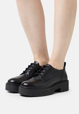 Chaussures en cuir noir avec un design à lacets, dotées d'une semelle épaisse noire et de détails de couture subtils. Texture lisse avec un bout arrondi.