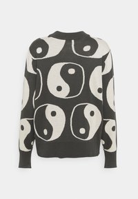 Zwart-witte trui met een yin-yang patroon. Gemaakt van zacht materiaal, met een ronde halslijn en geribde manchetten.