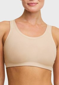 Beige nätidrottsbehå med breda axelband, rundad halsringning och en elastisk textur. Sömlös design för komfort och rörelsefrihet.