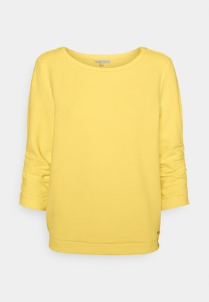 Geel gestructureerd, gebreid trui met lange mouwen, ronde halslijn en gerimpelde mouwen, weergegeven op een effen lichtgrijze achtergrond.