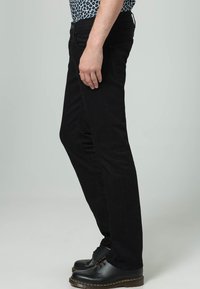 Svarta slim-fit jeans i denim, med en standard femfickorsdesign, subtil söm, och bärs med svarta snörskor.