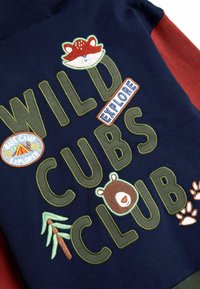 Tumesinine särk, millel on rohelise tikandiga tekst "WILD CUBS CLUB" ning loomade motiivid: rebane, karu ja puu, koos seikluse insigniaga.